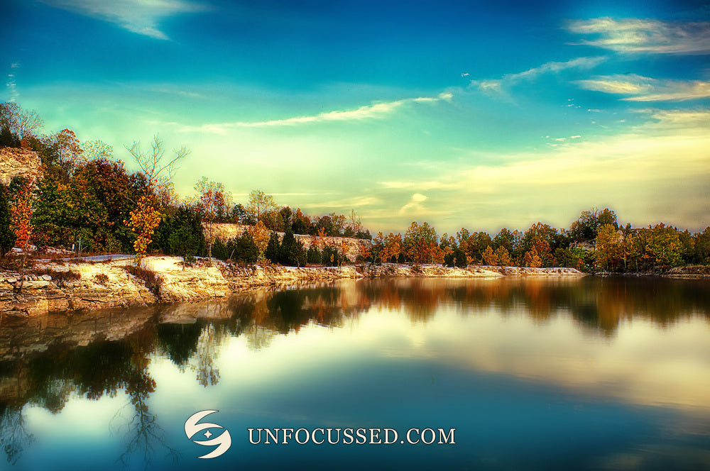 Glassy blue-green lake reflecting warm autumn trees and pale shoreline beneath a luminous sky at Klondike Park.