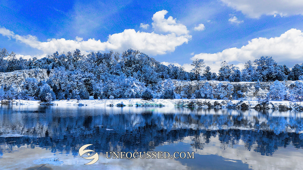 Blue-and-white artistic treatment of trees, rocky shoreline, clouds, and reflections at Klondike Park lake.