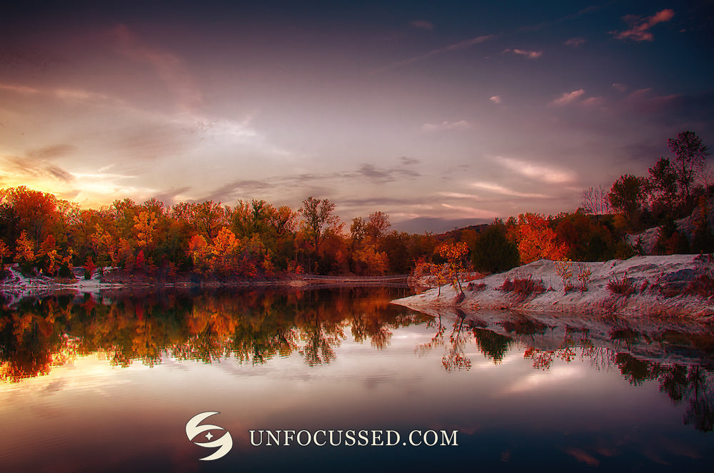 Soft sunrise over autumn trees and a pale rocky bank reflected in Klondike Park lake.
