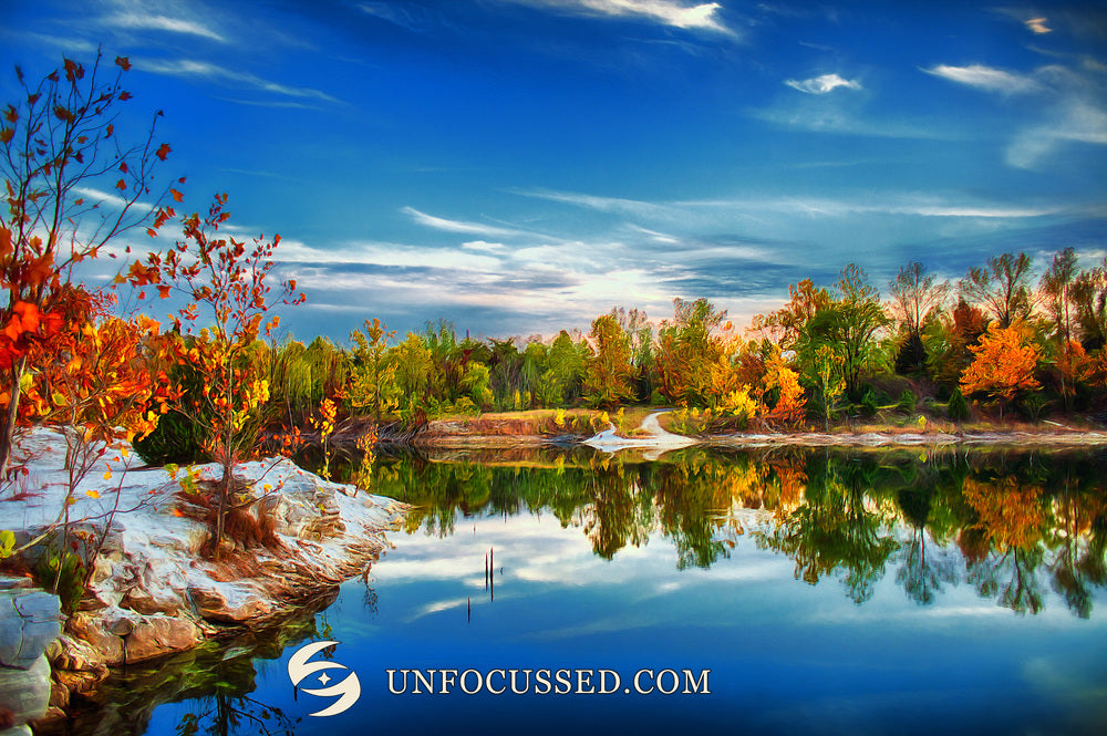 Painterly orange foliage beside pale shoreline and a reflective blue lake under streaked clouds at Klondike Park.