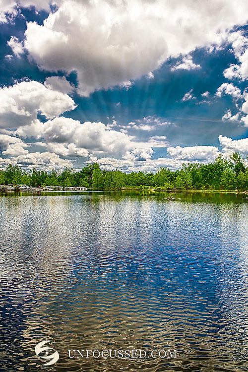 Puffy white clouds over a distant green shoreline and rippled blue water in a vertical Klondike Park photograph.