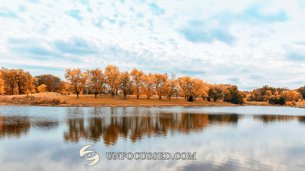 Orange Herbstbäume spiegeln sich im See von Broemmelsiek Park unter hellblauem Himmel und weichen Wolken.