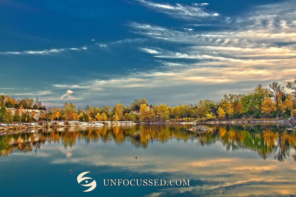 Strukturierte blaugraue Wolken über goldenen Herbstbäumen und glatter Seespiegelung in Klondike Park.