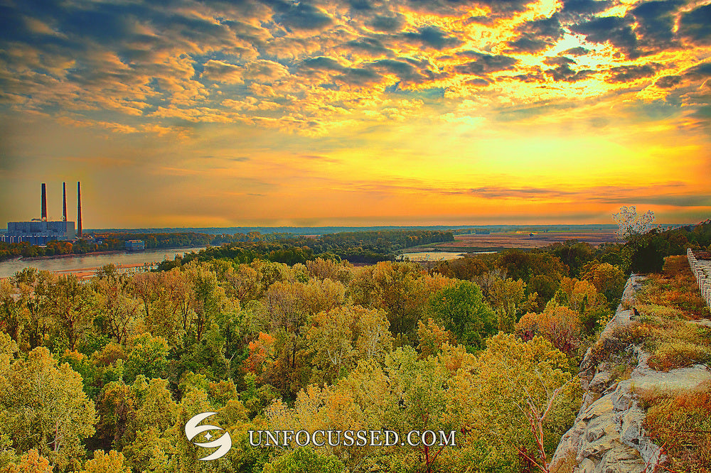 Goldener Himmel über bewaldetem Tal und fernen Industrieschornsteinen mit felsigem Aussichtsrandsaum in Klondike Park.